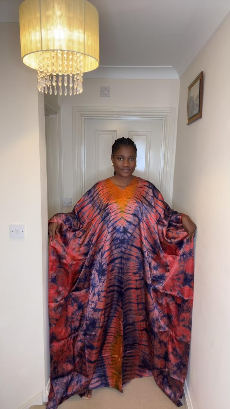 May include: A vibrant, tie-dye caftan in shades of orange, red, and blue. The loose-fitting garment features a V-neck and wide sleeves. The fabric has a flowing drape, creating a comfortable and stylish look.