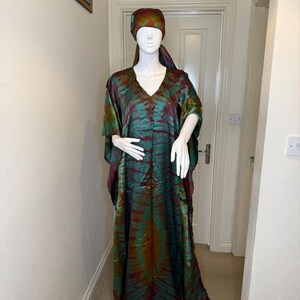 May include: A long, flowing, tie-dye dress and matching headscarf in shades of green, red, and gold. The dress has a V-neck and wide sleeves. The outfit is displayed on a mannequin.
