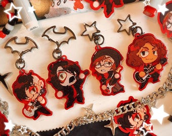 May include: A collection of red and black acrylic keychains featuring cartoon musicians with guitars. The keychains have silver-colored metal attachments, including bat and star shapes. A silver chain with star charms is also visible.