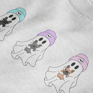 May include: Three cartoon ghost illustrations with French bulldog faces and holding teddy bears. Each ghost wears a beanie with a bat symbol. The beanies are light blue, lavender, and pink. The ghosts are on a white background.