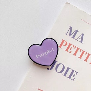 May include: A purple heart-shaped phone grip with a black border. The grip has the word "Purple!" written in white text.