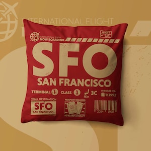 May include: A square red throw pillow featuring a vintage-style travel graphic with the text SFO SAN FRANCISCO, flight 415, terminal 1, class 1, seat 3C, and luggage number H1991. The design includes a passport icon and a barcode with the years 2004 and 1998.