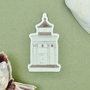 May include: A die-cut sticker featuring a detailed line drawing of a classical building with columns, a central door, and a roof lantern with a small yellow light. The illustration uses black ink outlines on a white background with subtle shading.