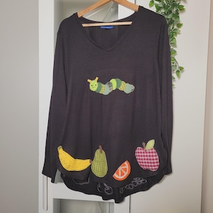 May include: Black long-sleeved shirt with a green caterpillar, a yellow banana, a green pear, a red apple, and an orange slice appliqué.