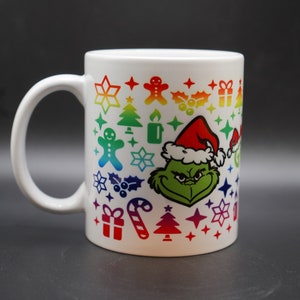 May include: White ceramic mug with a colorful design featuring the Grinch wearing a Santa hat and surrounded by Christmas icons like snowflakes, candy canes, and Christmas trees.