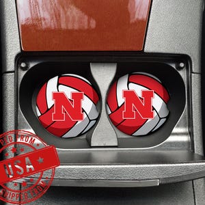 May include: Two car coasters with a red and white volleyball design and a large red "N" logo. The coasters are in a car's cup holders. The image also includes a red stamp that says "SHIPPED FROM USA".