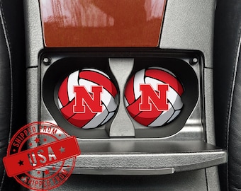 May include: Two car coasters with a red and white volleyball design and a large red "N" logo. The coasters are in a car's cup holders. The image also includes a red stamp that says "SHIPPED FROM USA".