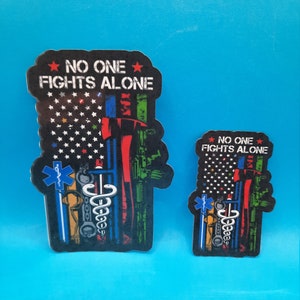 May include: Two stickers with an American flag design and the text "No One Fights Alone". The stickers feature a variety of symbols representing different professions, including a police badge, a firefighter's axe, a medical caduceus, and a military rifle.