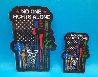 May include: Two stickers with an American flag design and the text "No One Fights Alone". The stickers feature a variety of symbols representing different professions, including a police badge, a firefighter's axe, a medical caduceus, and a military rifle.