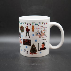 May include: White ceramic mug with a colorful design featuring images and text from the movie Home Alone. The design includes a Christmas tree, a wreath, a string of lights, a map, and a photo of Kevin McCallister.