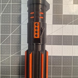 May include: A black and orange lightsaber hilt, featuring a cylindrical design with orange accents. The hilt has a series of orange rectangular and vertical stripe details. The lightsaber is made of a 3D printed material.