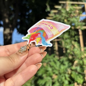 May include: A die-cut sticker featuring a pink bag labeled "Dummy Worms" overflowing with colorful, multi-colored fuzzy worm candies. The illustration includes individual red, blue, yellow, and green worm shapes with small white eyes spilling out.