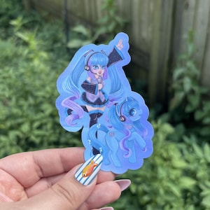 May include: A die-cut sticker featuring a blue-haired anime character with a headset and microphone, standing next to a blue pony with matching hair and a headset. The character wears a black and white outfit, and the pony has the number 01 on its flank.