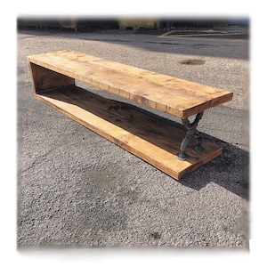 May include: A long wooden bench with a shelf underneath, supported by black metal pipe legs. The bench is made of reclaimed wood and has a rustic, industrial look.