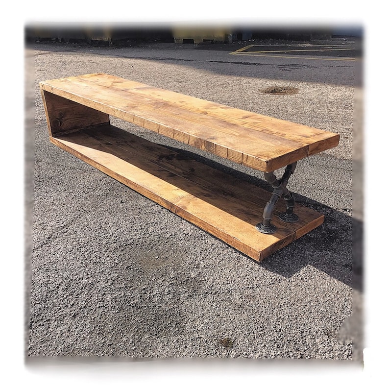May include: A long wooden bench with a shelf underneath, supported by black metal pipe legs. The bench is made of reclaimed wood and has a rustic, industrial look.