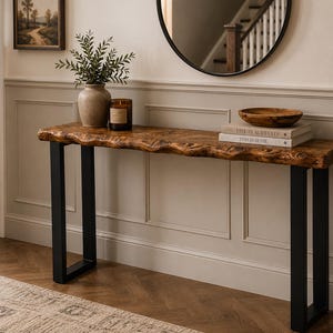 May include: A rustic console table with a live edge wooden top and black metal legs. The table is adorned with a vase of greenery, a candle, a wooden bowl, and books. The table is 152 cm long.