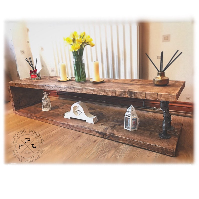 May include: A rustic wooden shelf unit with two shelves and black metal pipe legs. The shelf is decorated with a clock, a birdcage, a lantern, candles, and a vase of yellow daffodils. The shelf is labeled "Gooding Wooding Bespoke Handcrafted 2020".