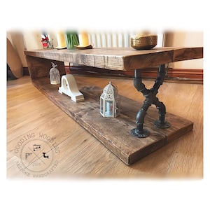 May include: Rustic wooden coffee table with a lower shelf and black metal pipe legs. The table has a distressed wood finish and is decorated with a birdcage, a clock, a lantern, and a bowl.