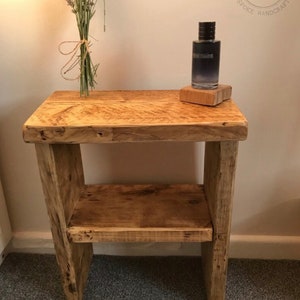 May include: A rustic wooden side table with a single shelf. The table is made of reclaimed wood and has a natural, weathered finish. The table is 61 cm tall and 41 cm wide.