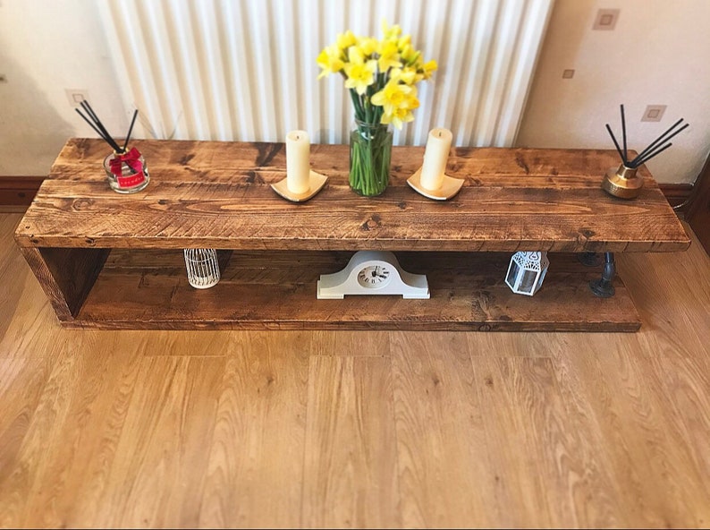 May include: A rustic wooden coffee table with a lower shelf. The table has a distressed brown finish and is decorated with candles, a clock, and a vase of yellow daffodils.