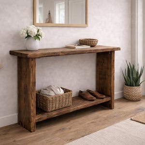 May include: A wooden console table with a lower shelf, holding a wicker basket and brown leather shoes. A white vase with white flowers sits on top. A canvas tote bag hangs on the wall.