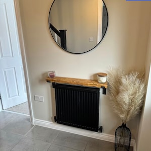 May include: A black radiator with a wooden shelf above it. The shelf is decorated with two candles and a dried pampas grass arrangement in a black wire vase.