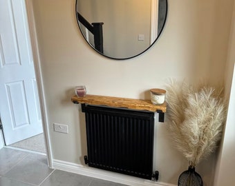 May include: A black radiator with a wooden shelf above it. The shelf is decorated with two candles and a dried pampas grass arrangement in a black wire vase.
