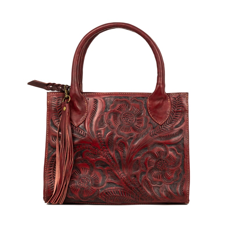 May include: A burgundy leather handbag with a floral embossed design. The bag features a top handle, a long tassel, and a zipper pull. The floral pattern is dark, creating a contrast with the burgundy leather. The bag is square-shaped.