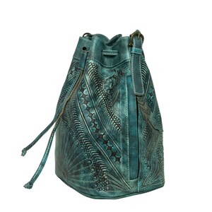 May include: A teal blue leather bucket bag with intricate embossed floral patterns. The bag has a drawstring closure and a long strap.