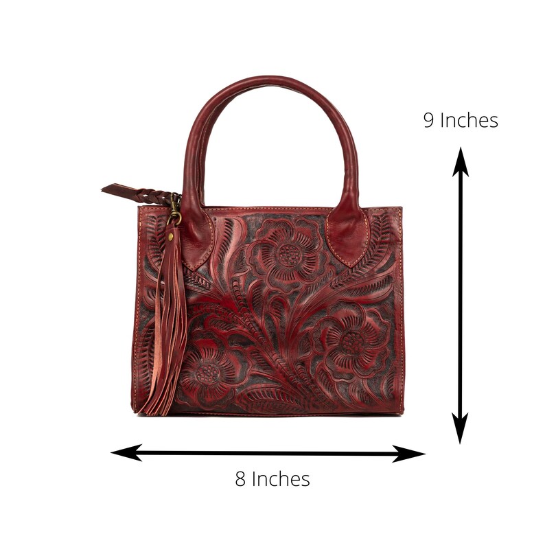May include: A burgundy leather handbag with a floral embossed design. The bag has a top handle, a tassel, and measures 9 inches tall and 8 inches wide.