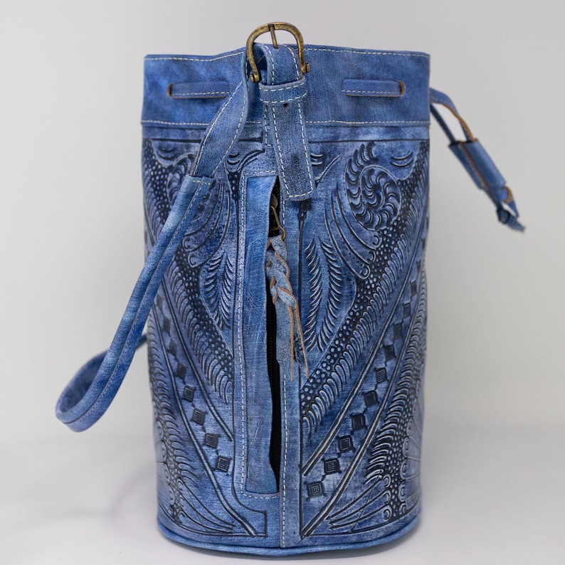 May include: A blue leather bucket bag with a floral embossed design and a drawstring closure. The bag has a long strap and a zippered pocket on the front.