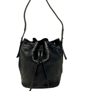 May include: A black leather bucket bag with a long strap and a drawstring closure. The bag has a textured, embossed design.