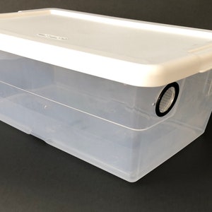 May include: A clear plastic storage container with a white lid. The container has two round holes in the lid, each with a black mesh screen.