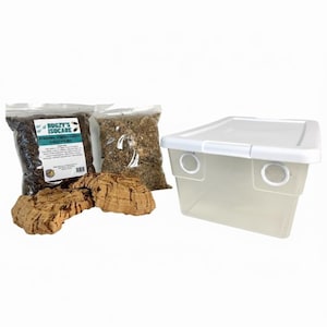 May include: A clear plastic terrarium with a white lid and ventilation holes, alongside bags of substrate and cork bark pieces. The bags contain dark and light brown materials. The label on one bag reads "Bugzy's Isocare".