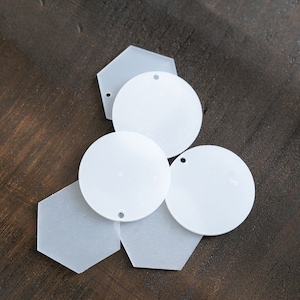 May include: Five white acrylic blank ornaments, two round, two hexagonal, and one star-shaped. The ornaments are perfect for crafting and personalization.