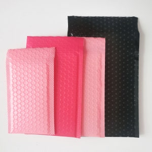 Könnte beinhalten: Vier Luftpolsterumschläge in verschiedenen Größen. Die Umschläge sind rosa, rot und schwarz. Die Umschläge bestehen aus Luftpolsterfolie.