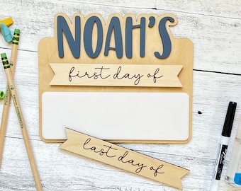 Op de afbeelding: Houten bord met de naam "Noah's" in blauwe letters. Het bord heeft een wit droog uitwisbaar oppervlak met de tekst "eerste dag van" en "laatste dag van" op houten banners.