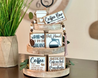 May include: A three-tiered wooden coffee bar display with decorative signs. The signs read "Coffee Bar," "Grab Life by the Beans," "Pot Head," "Coffee," and "Americano." The display includes a coffee cup, coffee pot, and wooden beads.
