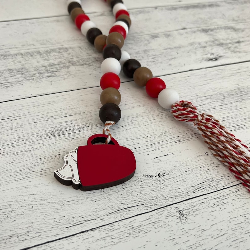 Hot cocoa themed wood bead garland. Dark brown, brown, red and white beads. Mug shaped tag with red and white tassel.