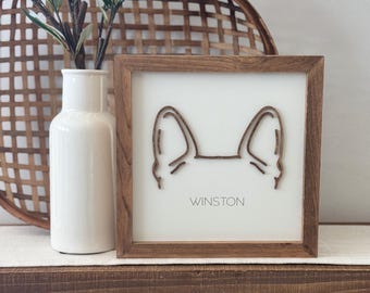 May include: A wooden framed sign with a white background and a cutout of a dog's ears. The text "Winston" is printed below the ears.