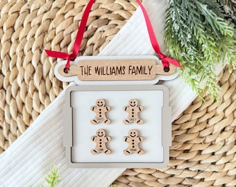 Puede incluir: Adorno navideño de madera con temática de hombre de jengibre. El adorno presenta un rodillo con el texto "The Williams Family" y cuatro hombres de jengibre con los nombres David, Emily, Liam y Noah.