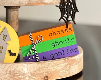 May include: A set of three wooden blocks stacked on top of each other. The blocks are painted in orange, green, and purple. The top block reads "ghosts", the middle block reads "ghouls", and the bottom block reads "& goblins".