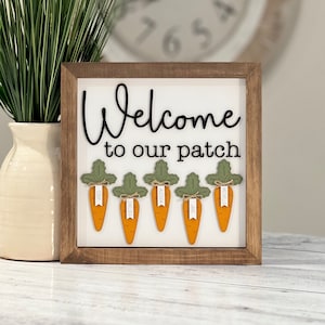 May include: Welcome to our patch sign with a wooden frame and six carrot decorations with names on each. The names are Cody, Chelsea, Alisha, Jake, Michelle.