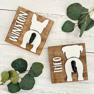 May include: Two wooden dog leash hooks with the names "Winston" and "Theo" written on them. Each hook features a white silhouette of a dog's rear end with a black hook.