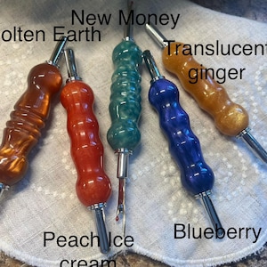 May include: A collection of five colorful seam rippers with metallic silver tips. The handles are in shades of orange, red, teal, blue, and gold, with names like "Molten Earth," "Peach Ice Cream," and "Translucent Ginger" written on the image.