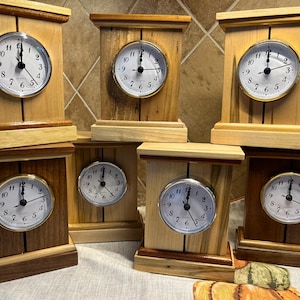 May include: Seven wooden clocks with different wood grain patterns and face designs. Each clock has a white face with black hands and black numbers. The clocks are arranged in a staggered formation.