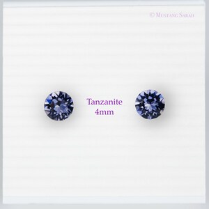 May include: Two round tanzanite gemstones, each 4mm in diameter, displayed on a white background. The gemstones are a deep blue-violet color and are faceted to catch the light. The text "Tanzanite 4mm" is in the center.