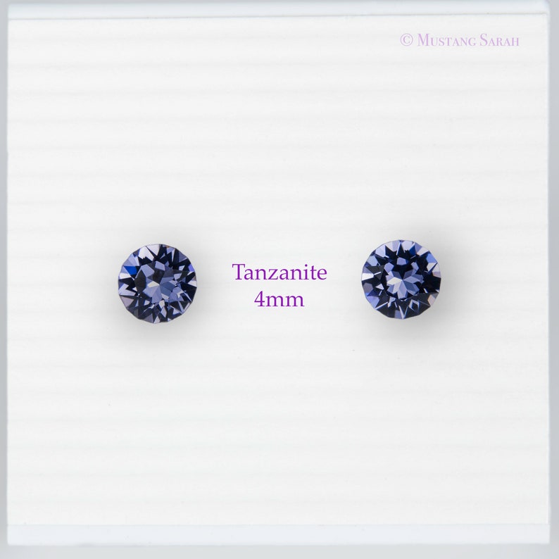 May include: Two round tanzanite gemstones, each 4mm in diameter, displayed on a white background. The gemstones are a deep blue-violet color and are faceted to catch the light. The text "Tanzanite 4mm" is in the center.