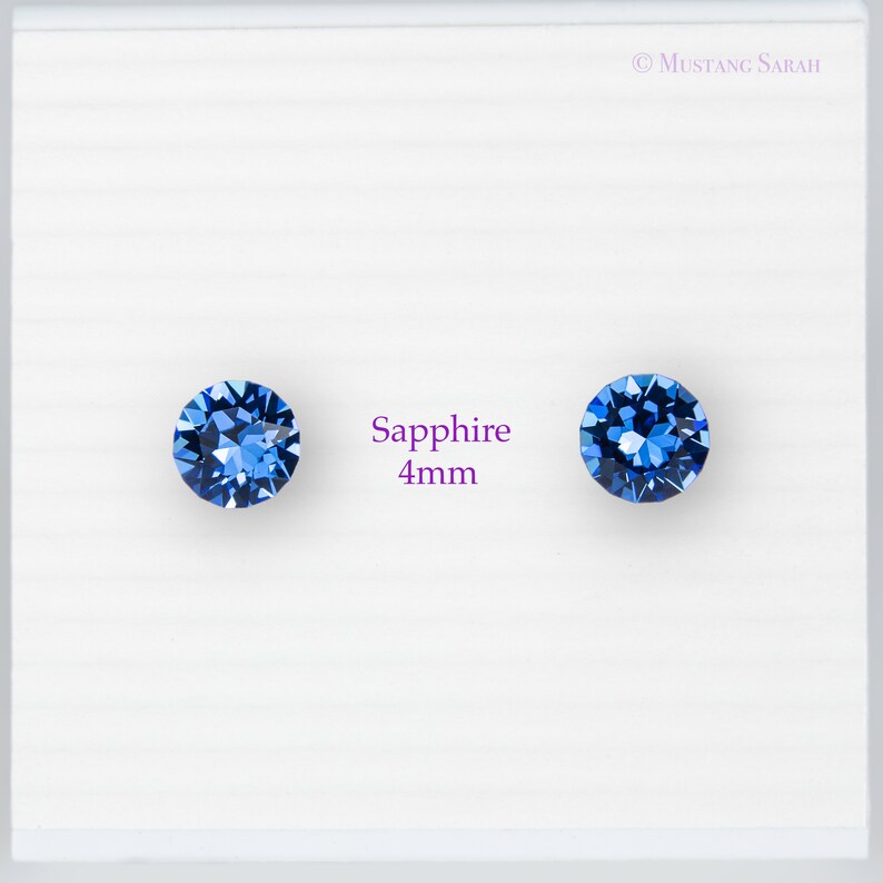 May include: Two round, faceted, sapphire blue gemstones, each 4mm in diameter, are displayed on a white background. The word "Sapphire" and the measurement "4mm" are printed in a purple font between the gemstones.
