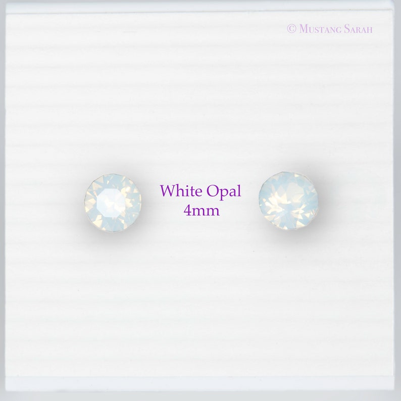 May include: Two white opal stud earrings, each 4mm in diameter, are displayed on a white background. The earrings have a round shape and a shimmering, iridescent appearance. The text "White Opal 4mm" is next to the earrings.